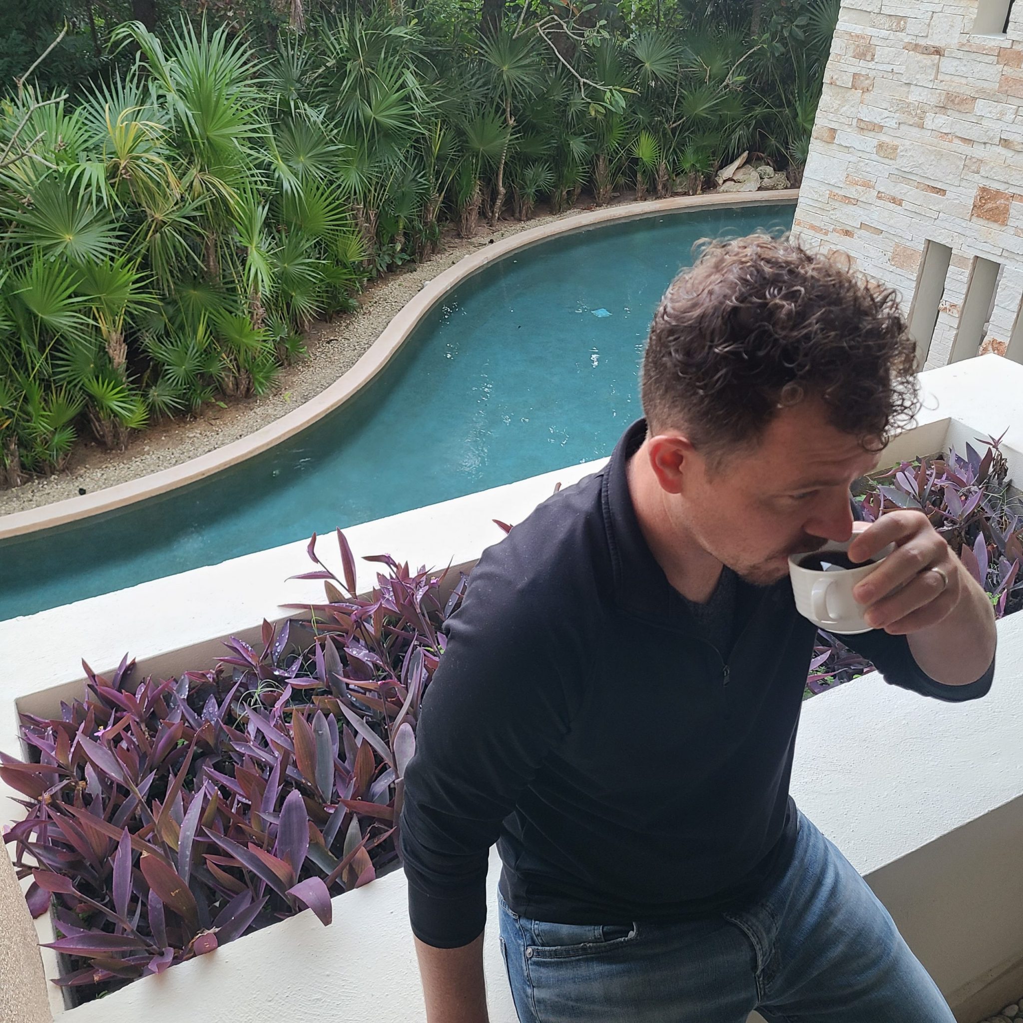 Jason on patio drinking coffee with pool below