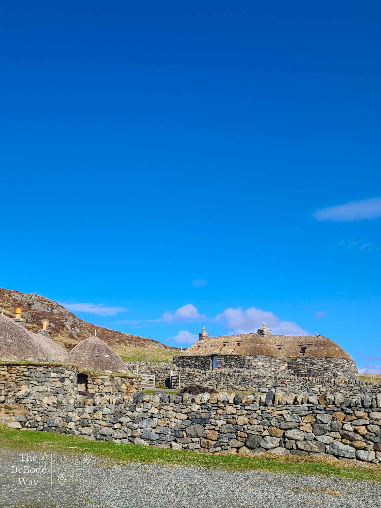 Stone blackhouse village with thatched roofs against a blue sky