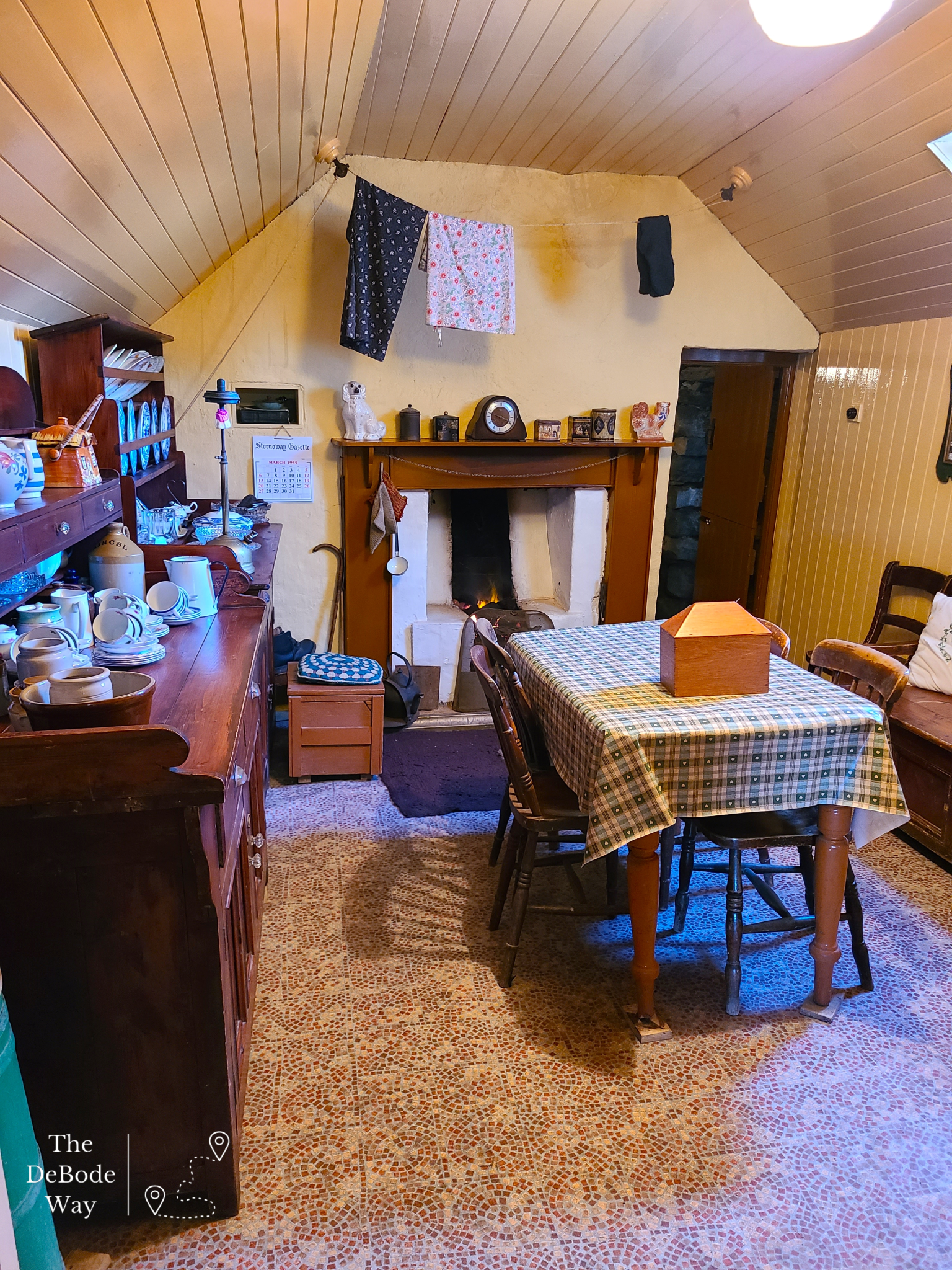 Yellow painted wood paneling, fireplace, kitchen table, wooden sideboard with dishes inside a blackhouse