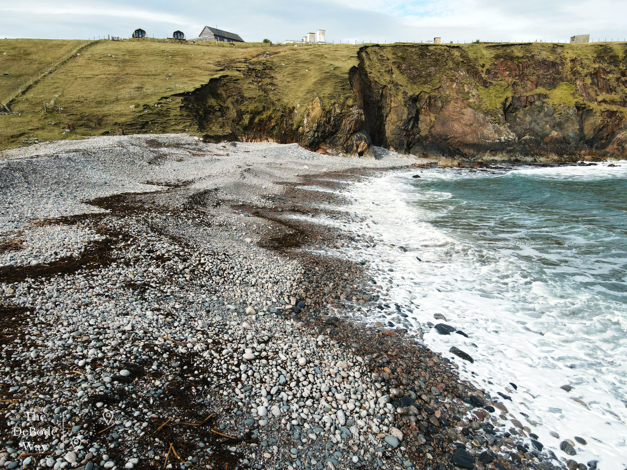 Waves crashing on rocky beach with cliff rising behind - houses atop the cliff