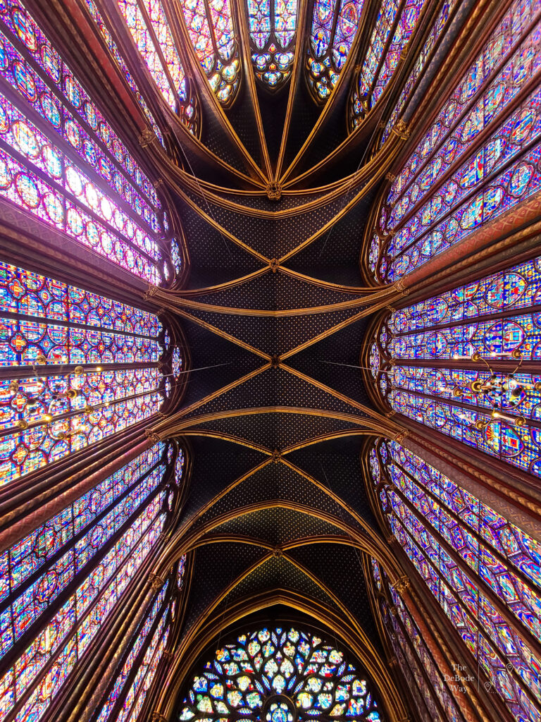 Colorful tall stained glass windows, blue ceiling with gold stars, and stained glass rose window at Saint-Chappelle Paris