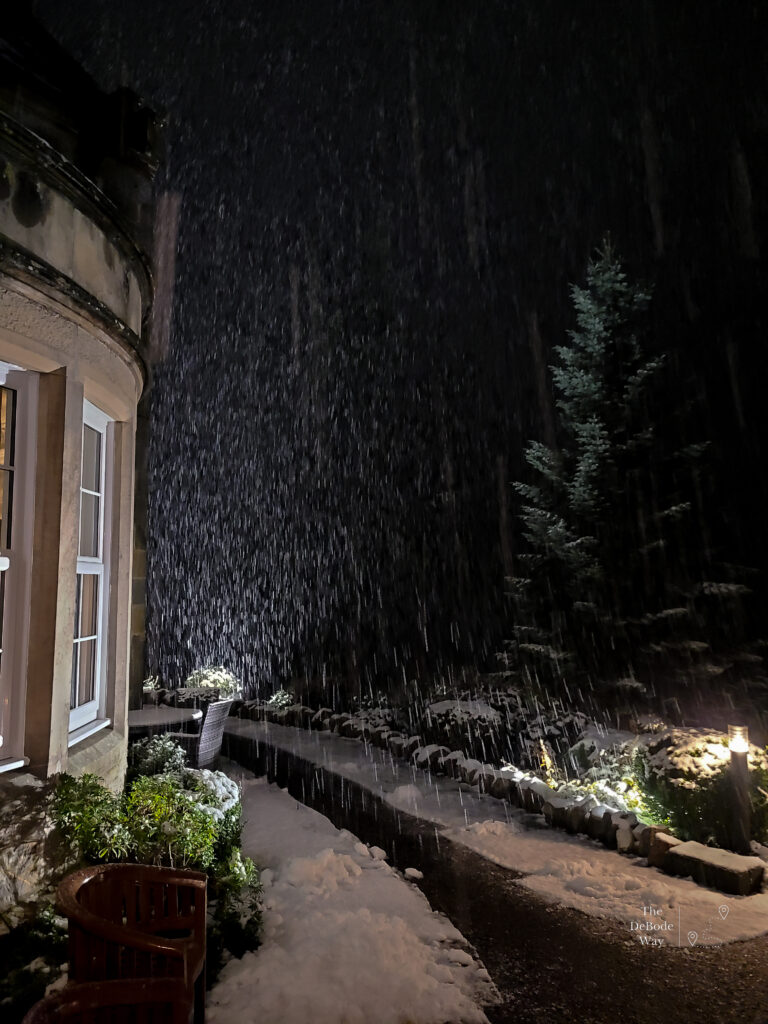 Snow against a dark sky with a melted walkway next to a stone bay window