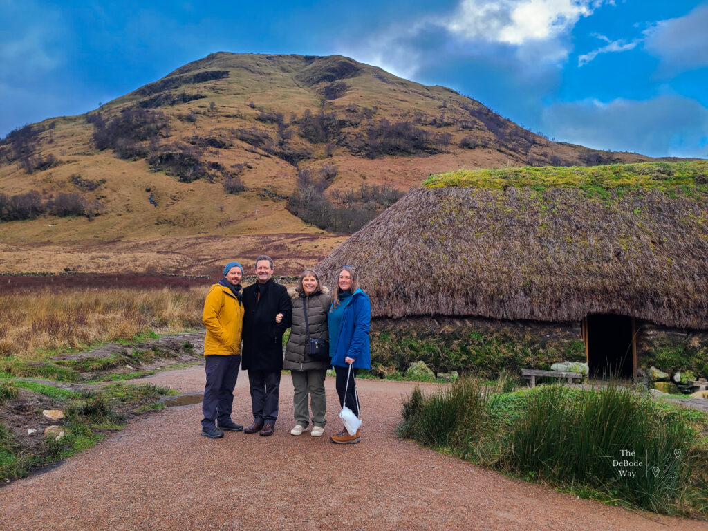 Jason, Doug, Sandy, and Tasha standing next to a turf house in Glen Coe with a mountain in the background