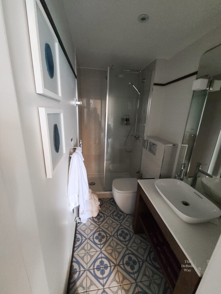 White, long skinny bathroom with blue painted tile floor and glass shower at the Perle Oban Hotel