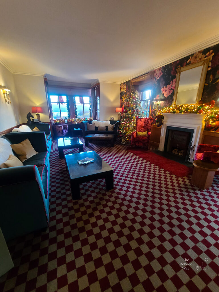 The parlor at Duisdale House - red and white checked carpet with green couches, white fireplace and big floral wallpaper, decorated for Christmas