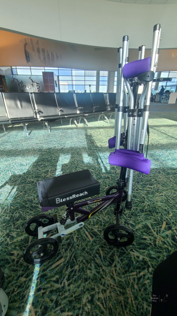 Purple knee scooter and folding crutches hanging from the handlebars at the airport
