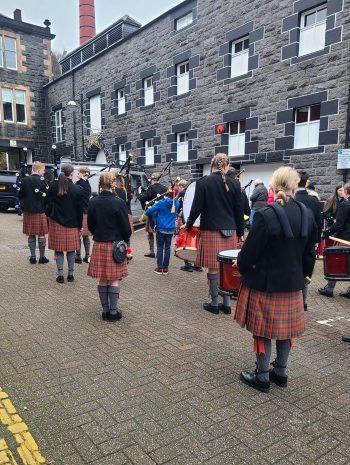 Oban High School pipe band lining up on the street next to Oban Disillery